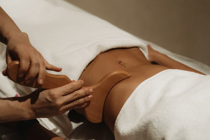 Masaje con herramienta de madera sobre el abdomen, con toallas blancas